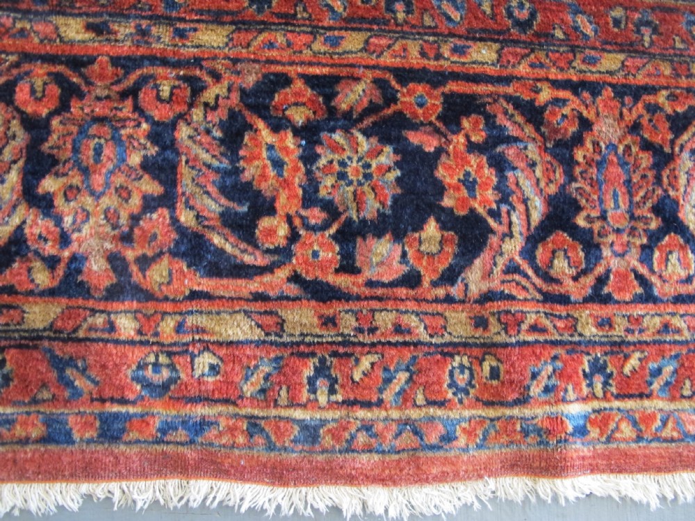 A large hand-knotted Persian Sarouk carpet featuring a dense floral pattern on a rose red field with a navy blue border. View VIII