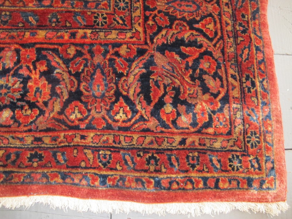 A large hand-knotted Persian Sarouk carpet featuring a dense floral pattern on a rose red field with a navy blue border. View IX