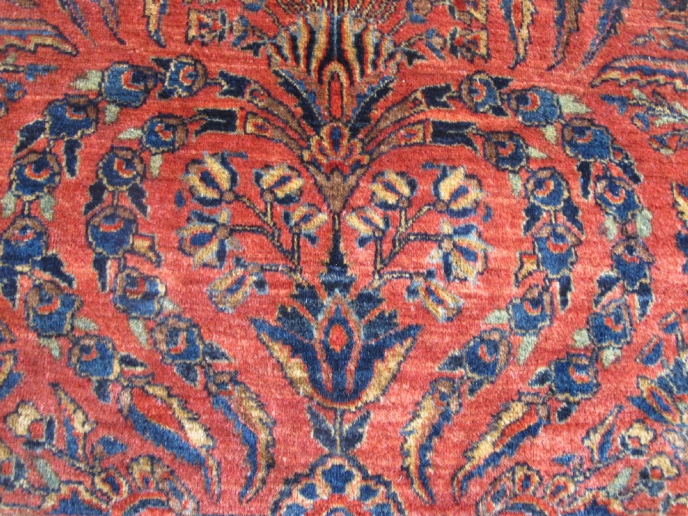 A large hand-knotted Persian Sarouk carpet featuring a dense floral pattern on a rose red field with a navy blue border. View X