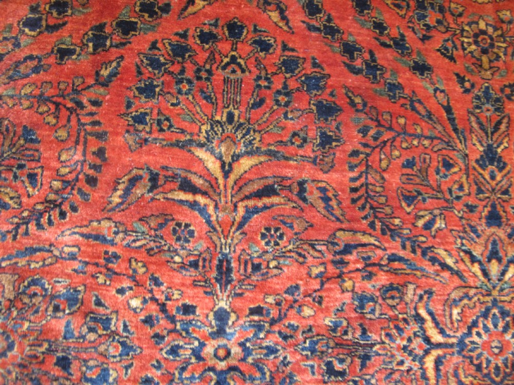 A large hand-knotted Persian Sarouk carpet featuring a dense floral pattern on a rose red field with a navy blue border. View XII