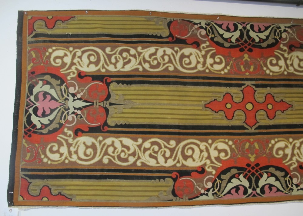 A long horizontal European wool tapestry panel featuring ornate scrolling foliage, geometric motifs, and metallic thread detailing in tones of red, olive, and beige. View II
