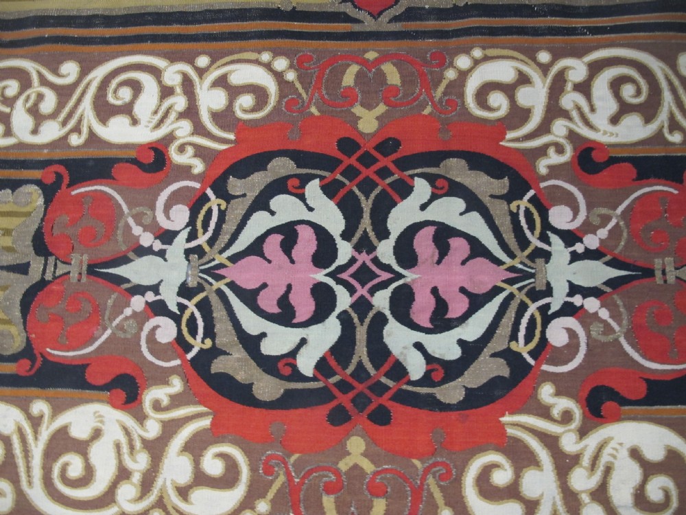 A long horizontal European wool tapestry panel featuring ornate scrolling foliage, geometric motifs, and metallic thread detailing in tones of red, olive, and beige. View III