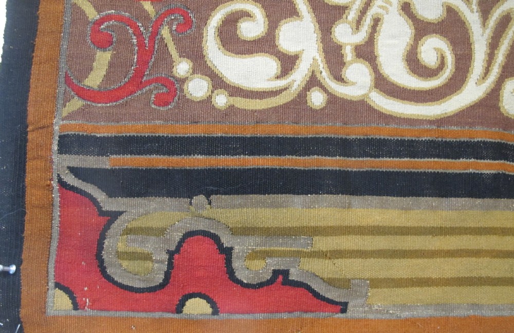 A long horizontal European wool tapestry panel featuring ornate scrolling foliage, geometric motifs, and metallic thread detailing in tones of red, olive, and beige. View V