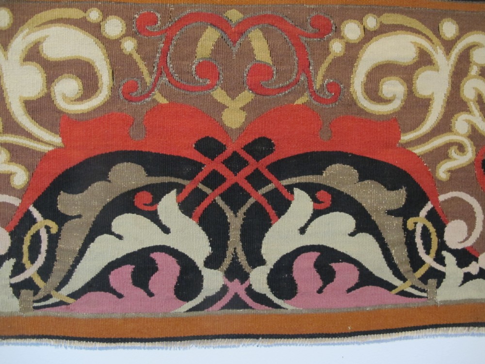 A long horizontal European wool tapestry panel featuring ornate scrolling foliage, geometric motifs, and metallic thread detailing in tones of red, olive, and beige. View VI