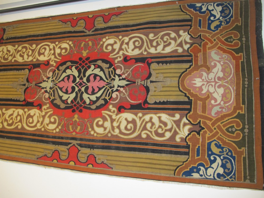 A long horizontal European wool tapestry panel featuring ornate scrolling foliage, geometric motifs, and metallic thread detailing in tones of red, olive, and beige. View X