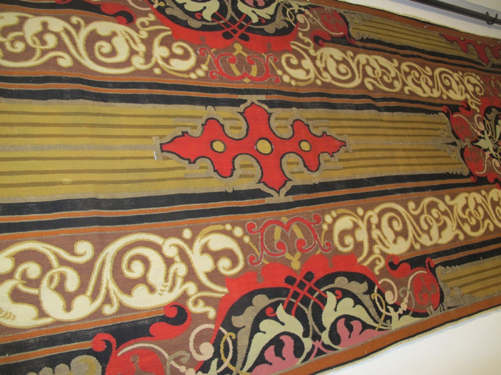 A long horizontal European wool tapestry panel featuring ornate scrolling foliage, geometric motifs, and metallic thread detailing in tones of red, olive, and beige. View XI