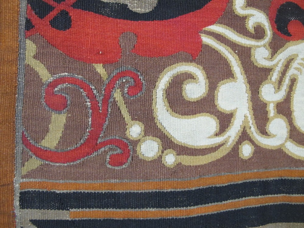 A long horizontal European wool tapestry panel featuring ornate scrolling foliage, geometric motifs, and metallic thread detailing in tones of red, olive, and beige. View XII