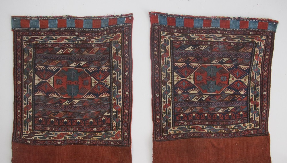 A pair of antique Caucasian Shahsavan soumac woven bags featuring geometric medallions in terracotta red, navy blue, and cream wool with decorative loops along the top edge.