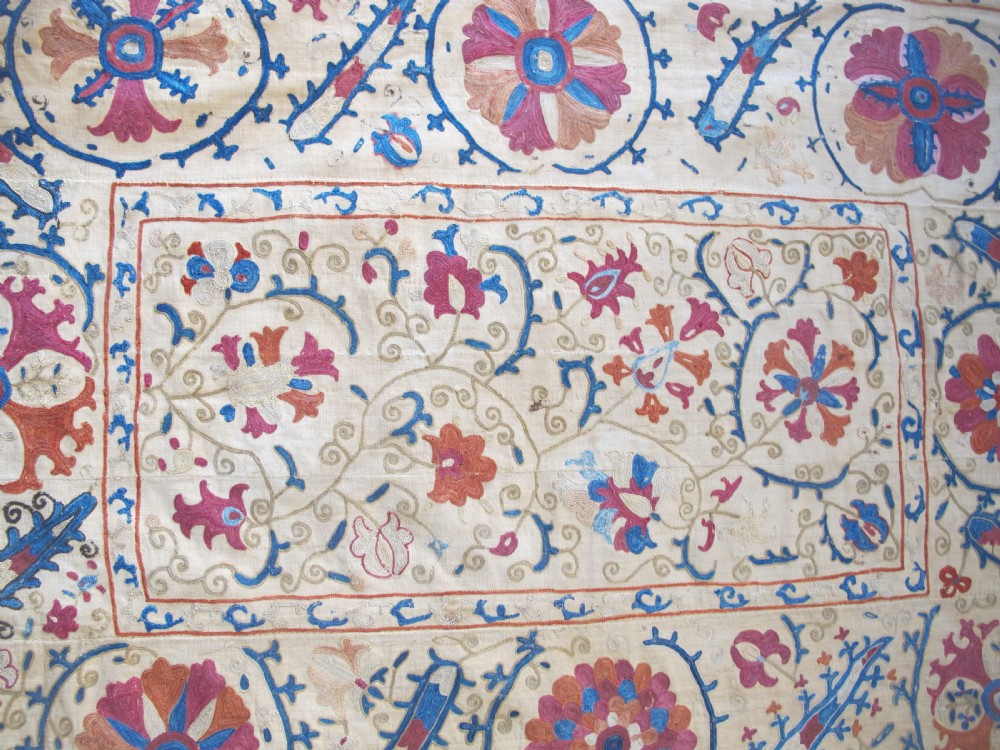 A rectangular hand-embroidered Uzbek silk textile panel featuring circular floral rosettes, vines, and leaf motifs in red, blue, and terracotta on a cream ground. View II