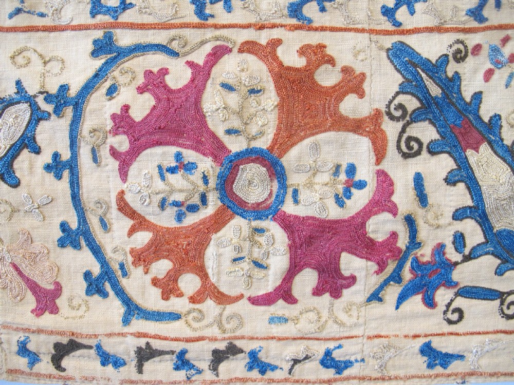 A rectangular hand-embroidered Uzbek silk textile panel featuring circular floral rosettes, vines, and leaf motifs in red, blue, and terracotta on a cream ground. View III