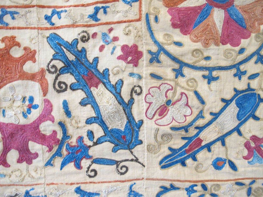 A rectangular hand-embroidered Uzbek silk textile panel featuring circular floral rosettes, vines, and leaf motifs in red, blue, and terracotta on a cream ground. View IV