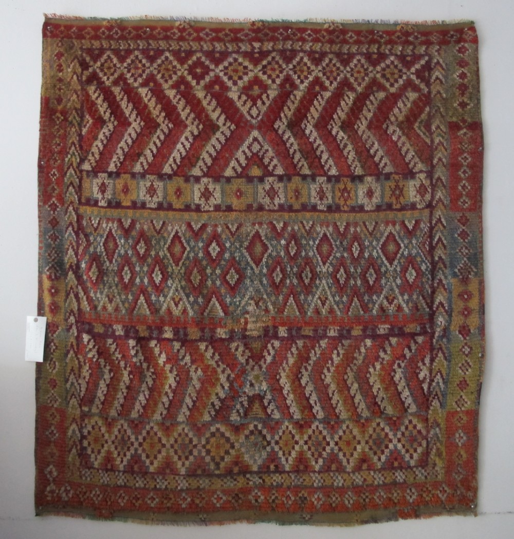 An antique rectangular Moroccan Glaoui rug featuring geometric diamond and chevron patterns in terracotta red, ochre, cream, and charcoal tones.