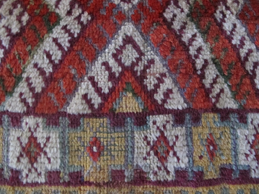 An antique rectangular Moroccan Glaoui rug featuring geometric diamond and chevron patterns in terracotta red, ochre, cream, and charcoal tones. View II