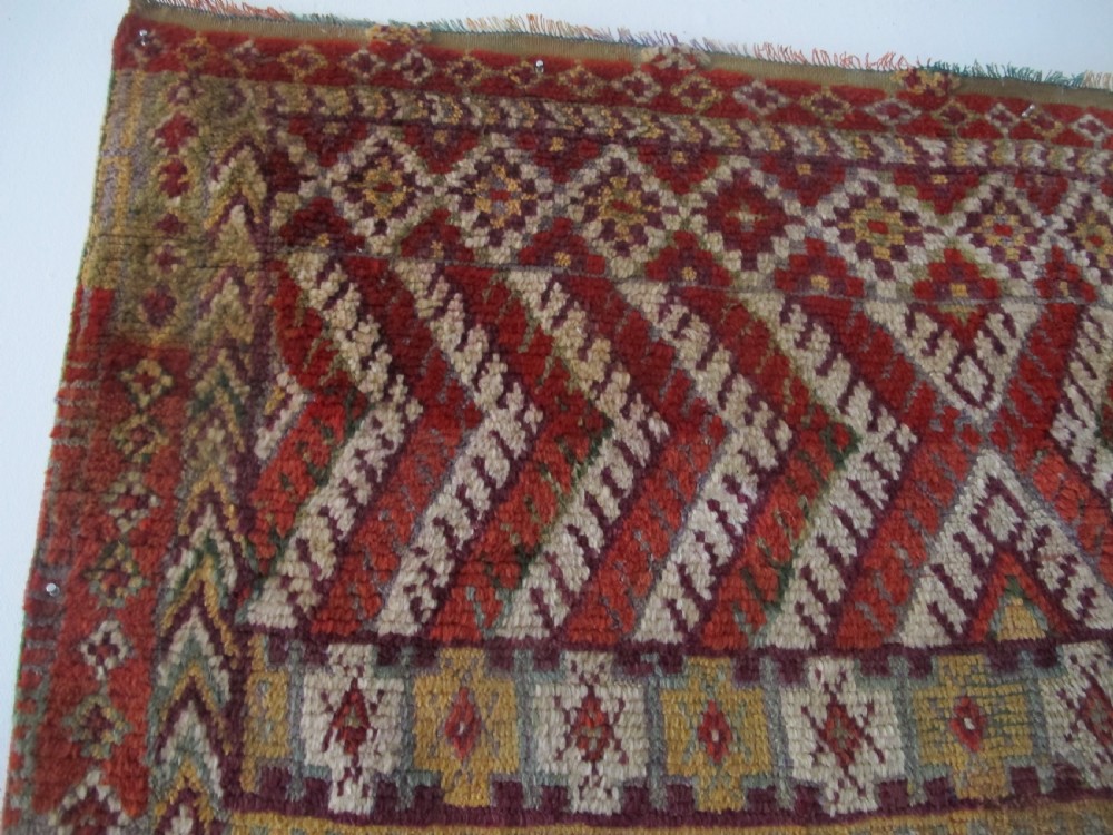 An antique rectangular Moroccan Glaoui rug featuring geometric diamond and chevron patterns in terracotta red, ochre, cream, and charcoal tones. View V