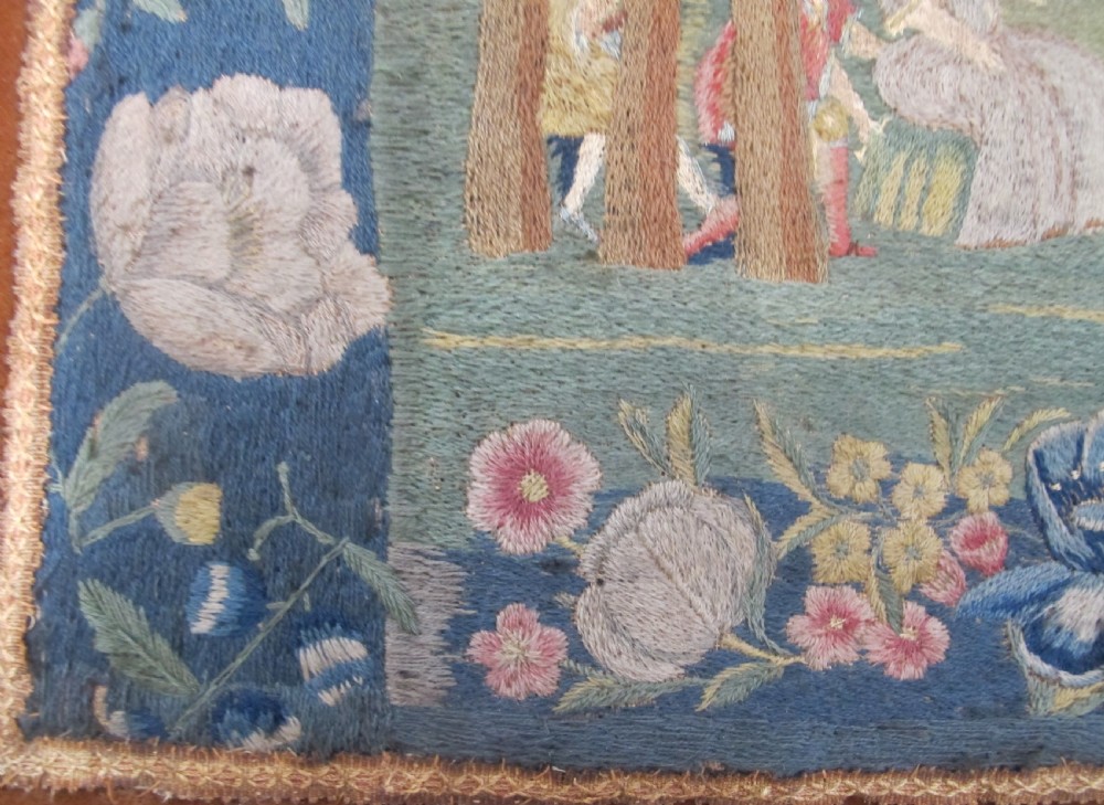 An antique square silk needlework panel displaying figurative pastoral scenes inside a wide floral border. View VII
