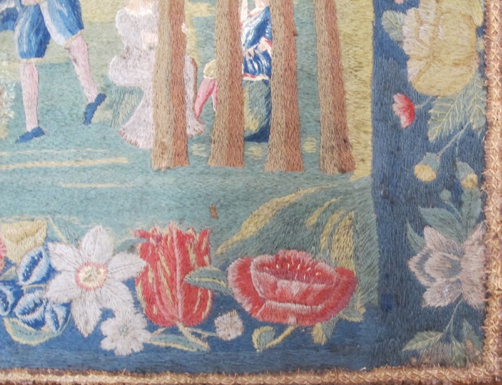 An antique square silk needlework panel displaying figurative pastoral scenes inside a wide floral border. View IX