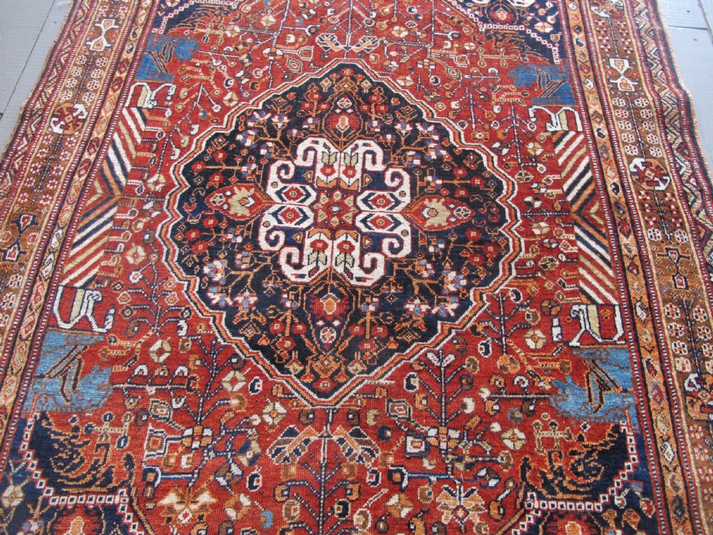 An antique Qashqai wool rug featuring a central diamond medallion, geometric tribal motifs, and intricate borders in shades of terracotta red, navy indigo, and cream. View II