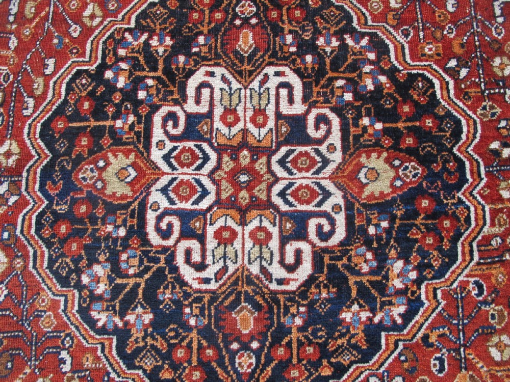 An antique Qashqai wool rug featuring a central diamond medallion, geometric tribal motifs, and intricate borders in shades of terracotta red, navy indigo, and cream. View III