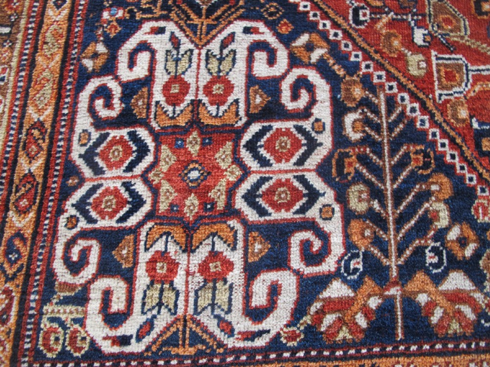 An antique Qashqai wool rug featuring a central diamond medallion, geometric tribal motifs, and intricate borders in shades of terracotta red, navy indigo, and cream. View IV