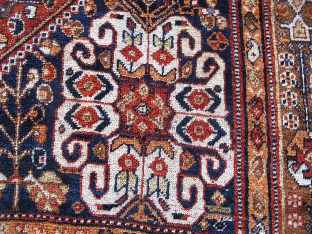 An antique Qashqai wool rug featuring a central diamond medallion, geometric tribal motifs, and intricate borders in shades of terracotta red, navy indigo, and cream. View VI