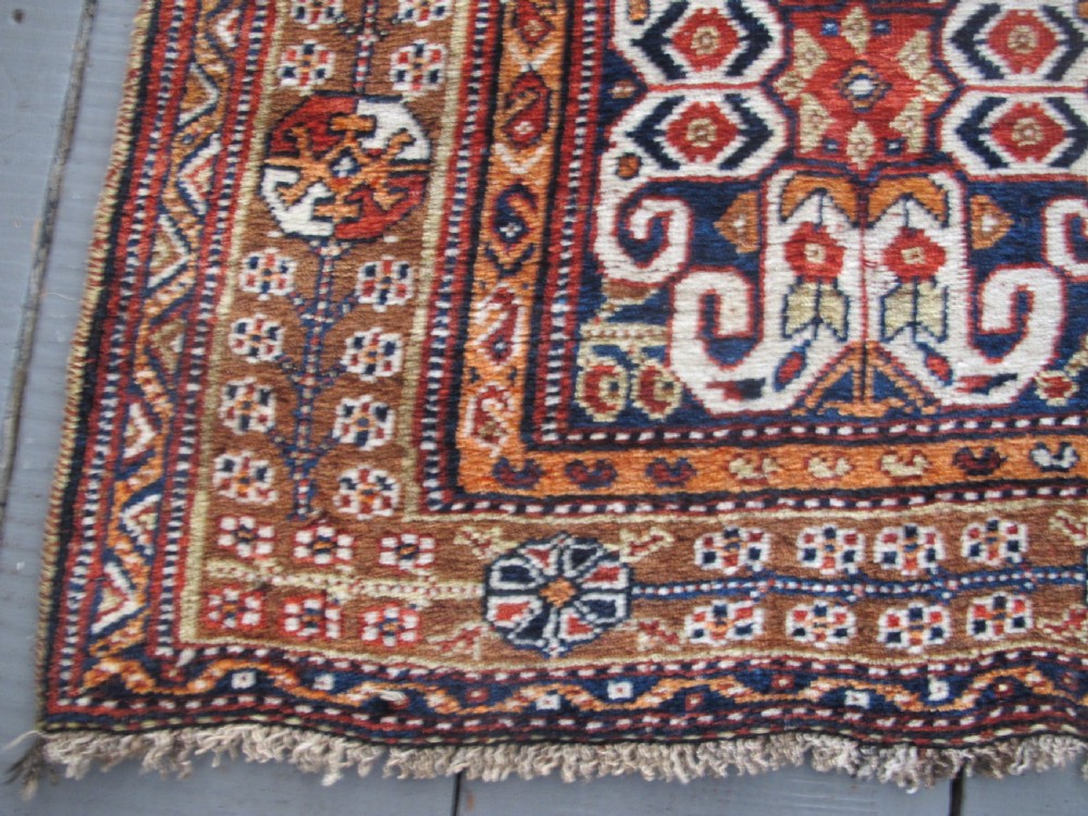 An antique Qashqai wool rug featuring a central diamond medallion, geometric tribal motifs, and intricate borders in shades of terracotta red, navy indigo, and cream. View VII