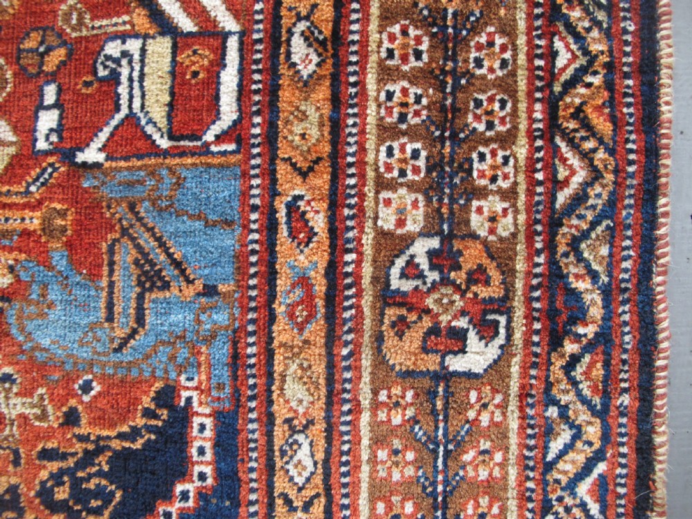 An antique Qashqai wool rug featuring a central diamond medallion, geometric tribal motifs, and intricate borders in shades of terracotta red, navy indigo, and cream. View VIII
