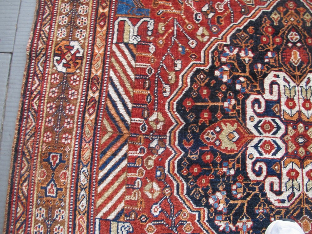 An antique Qashqai wool rug featuring a central diamond medallion, geometric tribal motifs, and intricate borders in shades of terracotta red, navy indigo, and cream. View IX