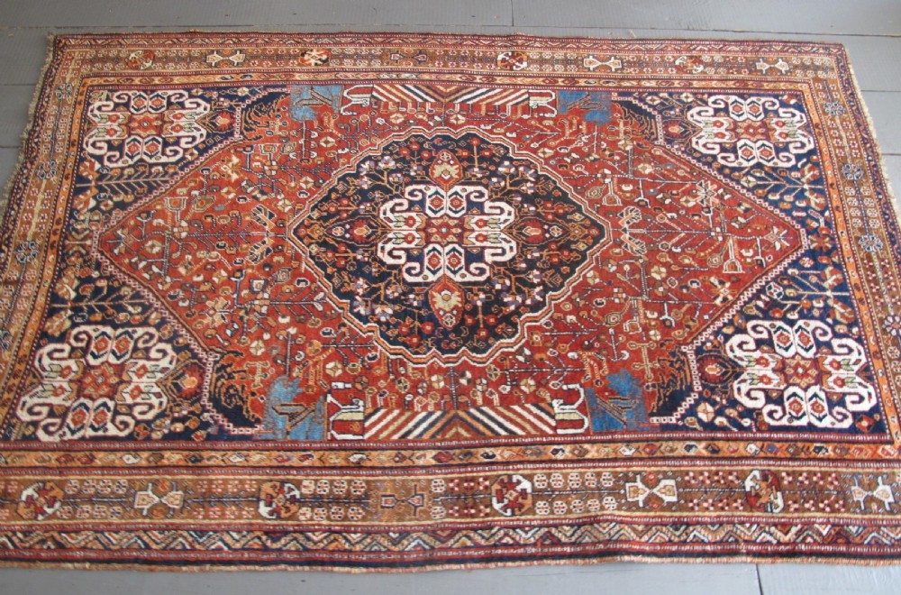 An antique Qashqai wool rug featuring a central diamond medallion, geometric tribal motifs, and intricate borders in shades of terracotta red, navy indigo, and cream. View XI