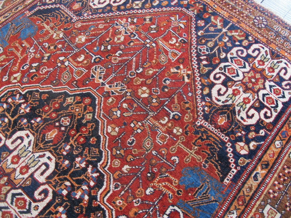 An antique Qashqai wool rug featuring a central diamond medallion, geometric tribal motifs, and intricate borders in shades of terracotta red, navy indigo, and cream. View XII