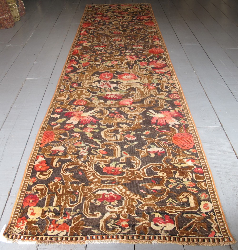 A long antique hand-knotted wool runner featuring red floral motifs and scrolling foliage against a dark brown background.