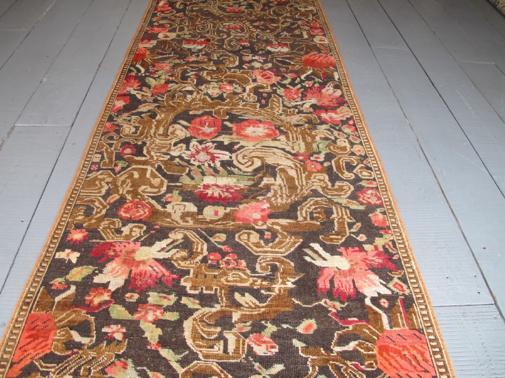 A long antique hand-knotted wool runner featuring red floral motifs and scrolling foliage against a dark brown background. View II