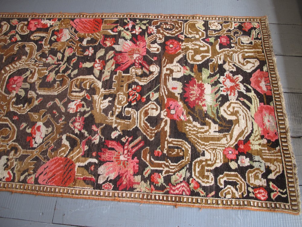 A long antique hand-knotted wool runner featuring red floral motifs and scrolling foliage against a dark brown background. View XIV