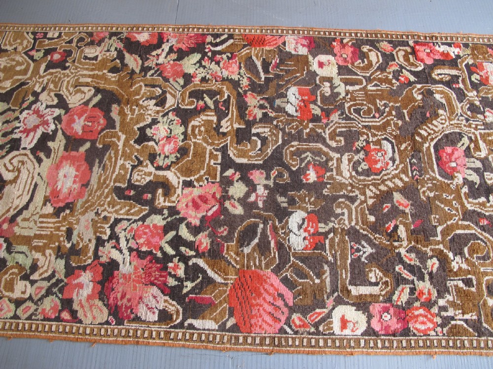 A long antique hand-knotted wool runner featuring red floral motifs and scrolling foliage against a dark brown background. View XV