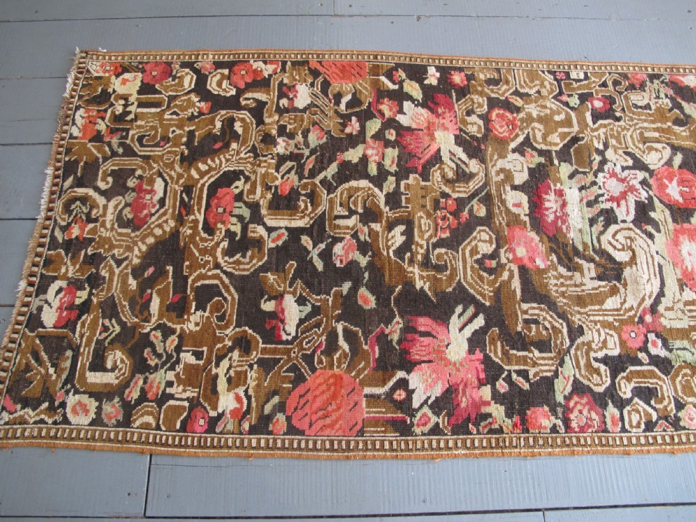 A long antique hand-knotted wool runner featuring red floral motifs and scrolling foliage against a dark brown background. View XVI