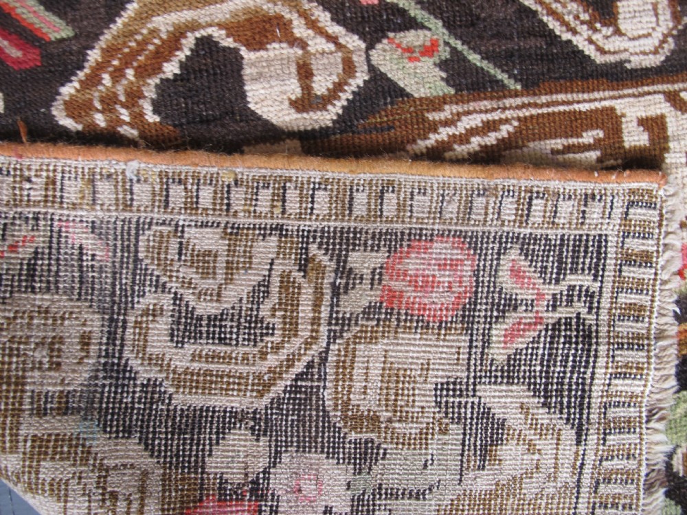 A long antique hand-knotted wool runner featuring red floral motifs and scrolling foliage against a dark brown background. View XVII