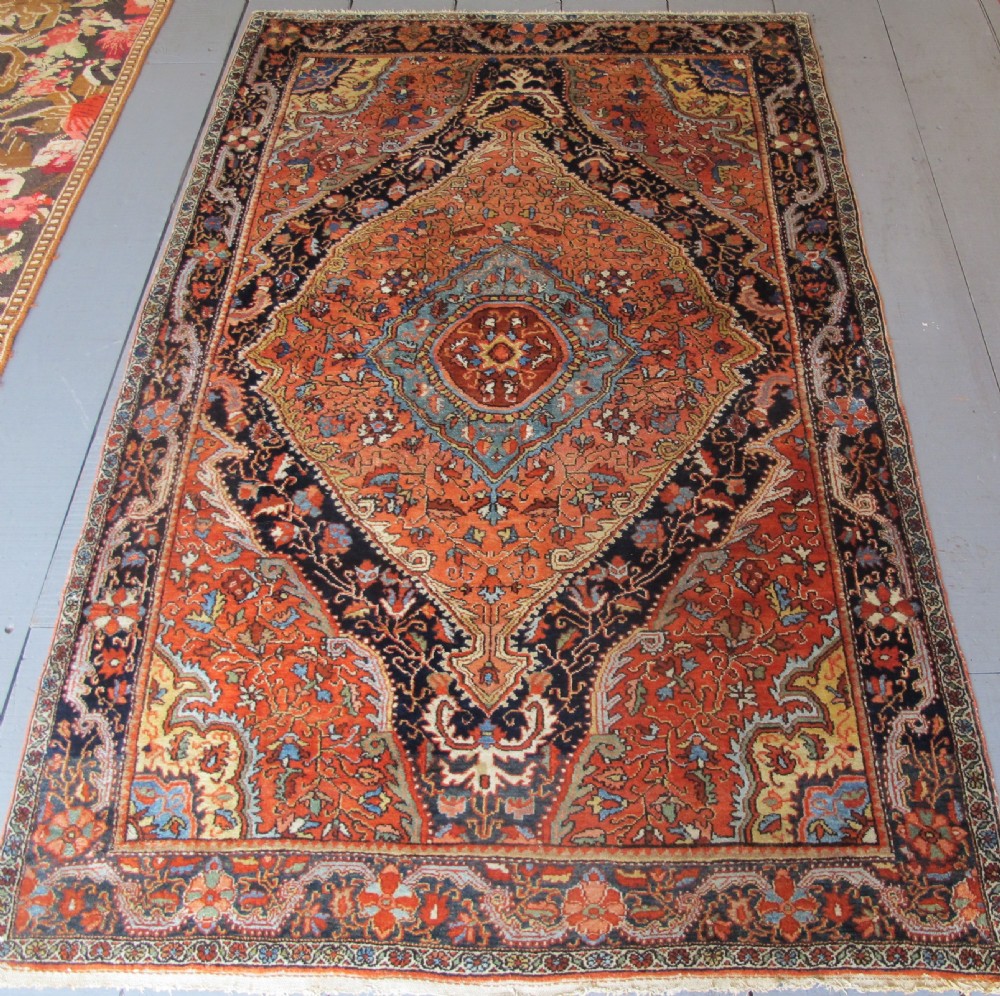 An antique Persian Jozan rug featuring a terracotta red field, central diamond medallion, dark navy spandrels, and intricate floral motifs.