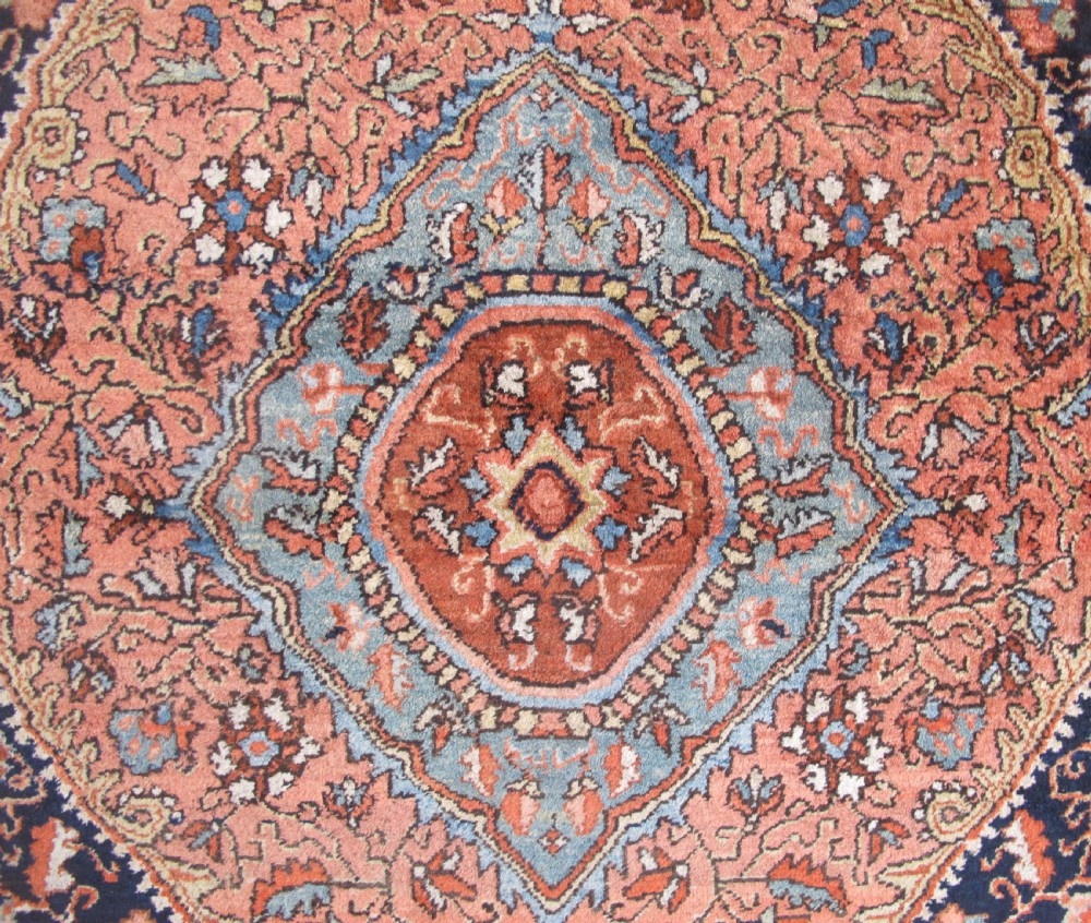 An antique Persian Jozan rug featuring a terracotta red field, central diamond medallion, dark navy spandrels, and intricate floral motifs. View VII