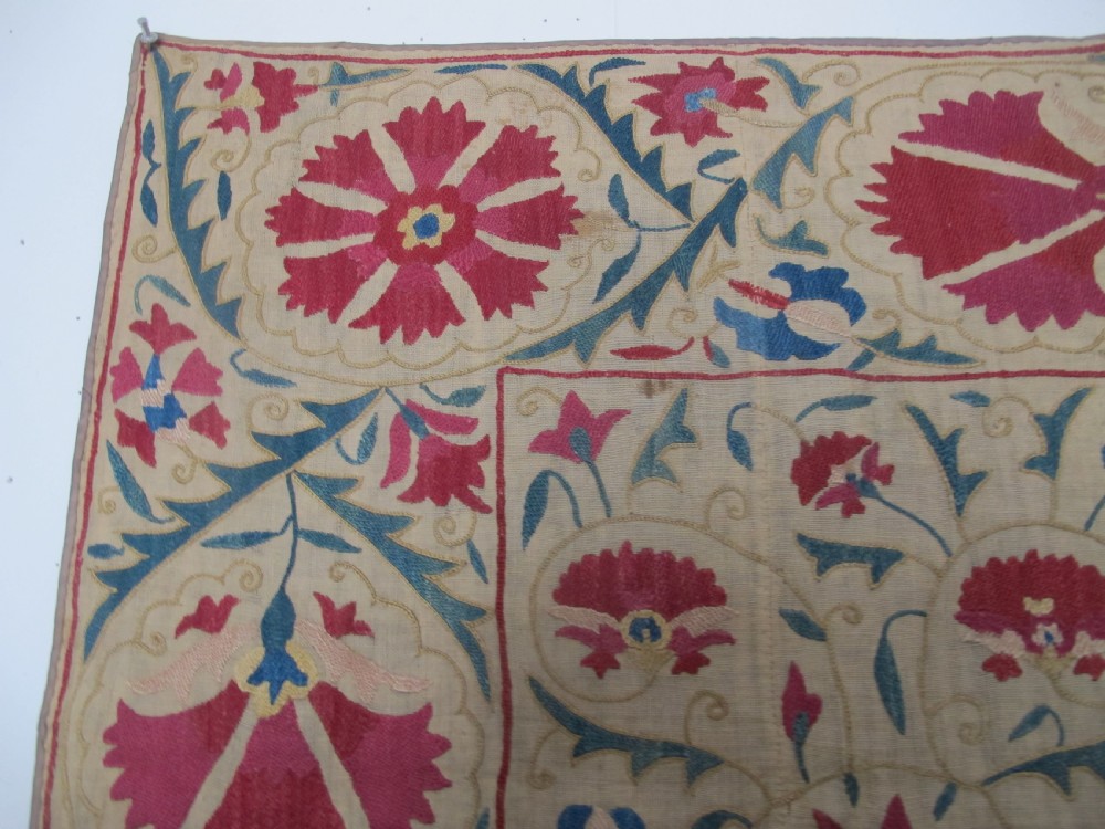 A rectangular antique silk-embroidered Suzani textile featuring crimson floral motifs and scrolling leaf borders on a beige cotton ground. View II