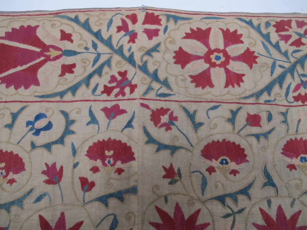 A rectangular antique silk-embroidered Suzani textile featuring crimson floral motifs and scrolling leaf borders on a beige cotton ground. View III
