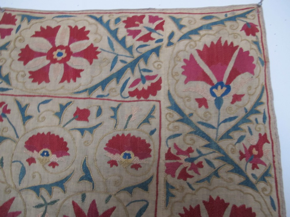 A rectangular antique silk-embroidered Suzani textile featuring crimson floral motifs and scrolling leaf borders on a beige cotton ground. View IV