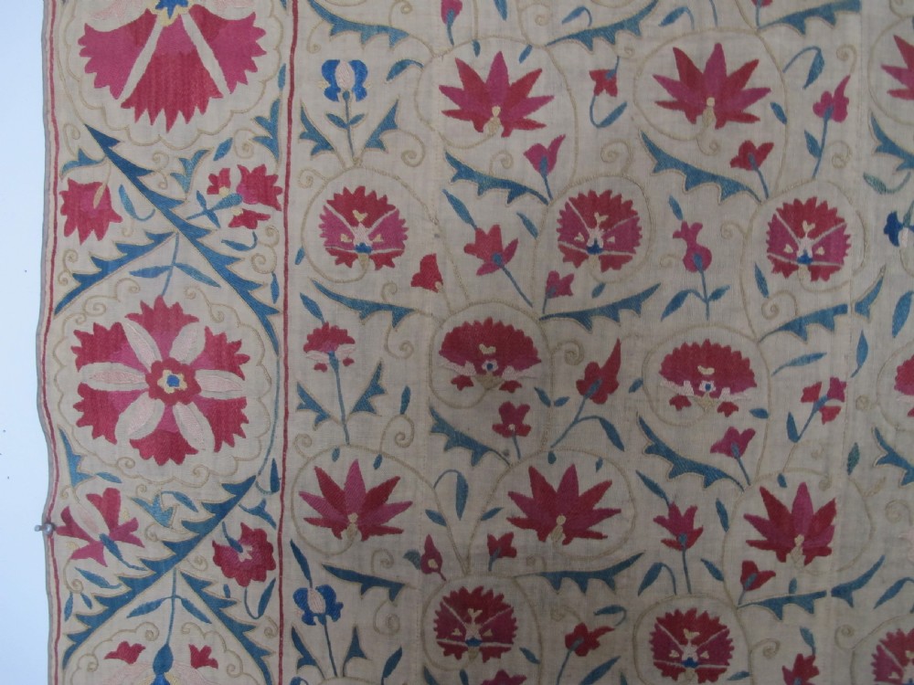 A rectangular antique silk-embroidered Suzani textile featuring crimson floral motifs and scrolling leaf borders on a beige cotton ground. View VI