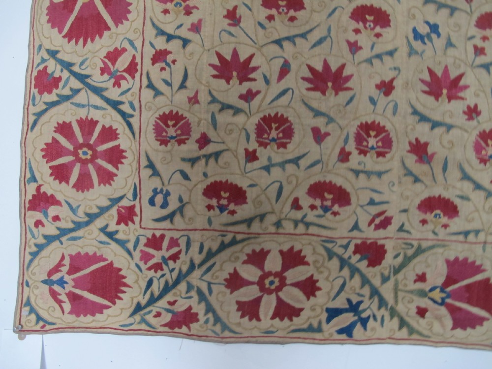 A rectangular antique silk-embroidered Suzani textile featuring crimson floral motifs and scrolling leaf borders on a beige cotton ground. View VII