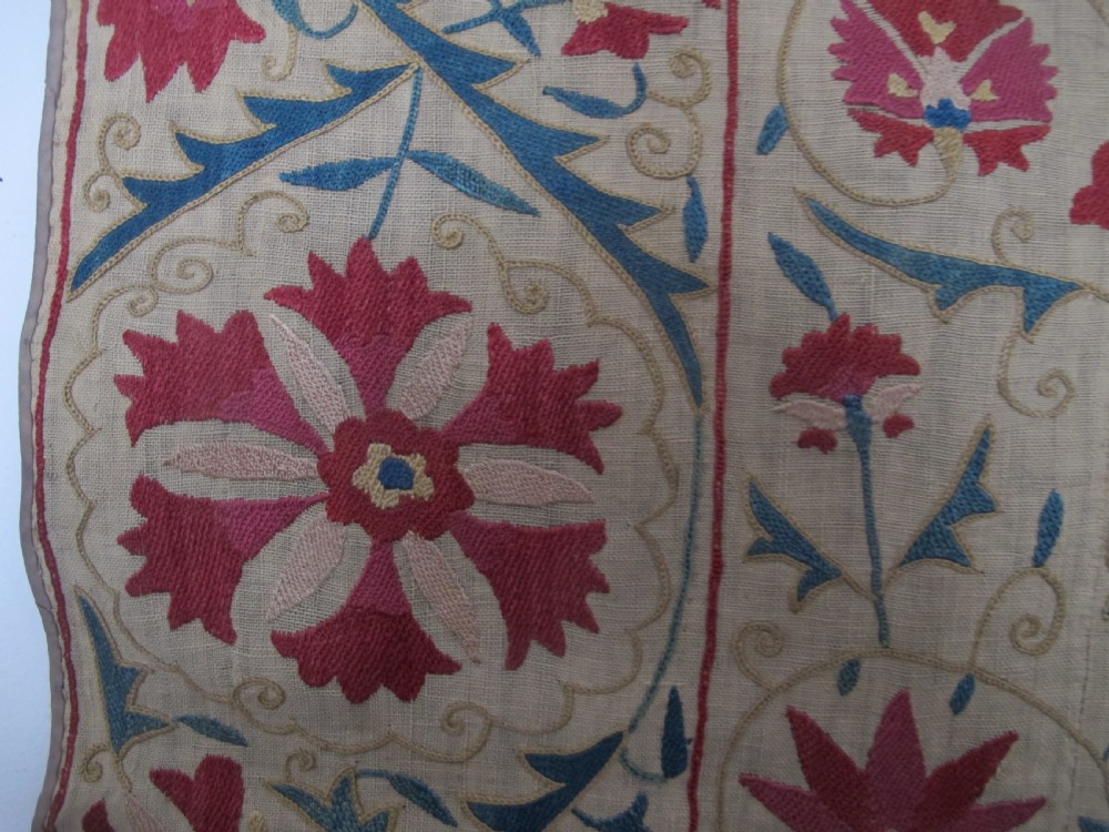 A rectangular antique silk-embroidered Suzani textile featuring crimson floral motifs and scrolling leaf borders on a beige cotton ground. View X