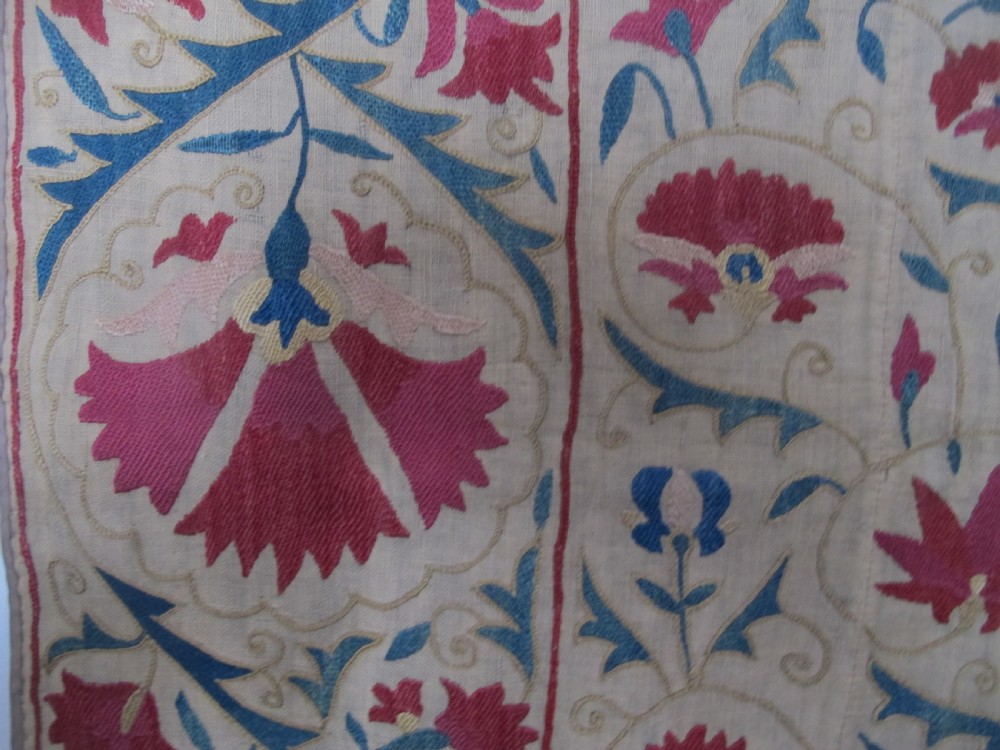 A rectangular antique silk-embroidered Suzani textile featuring crimson floral motifs and scrolling leaf borders on a beige cotton ground. View XI