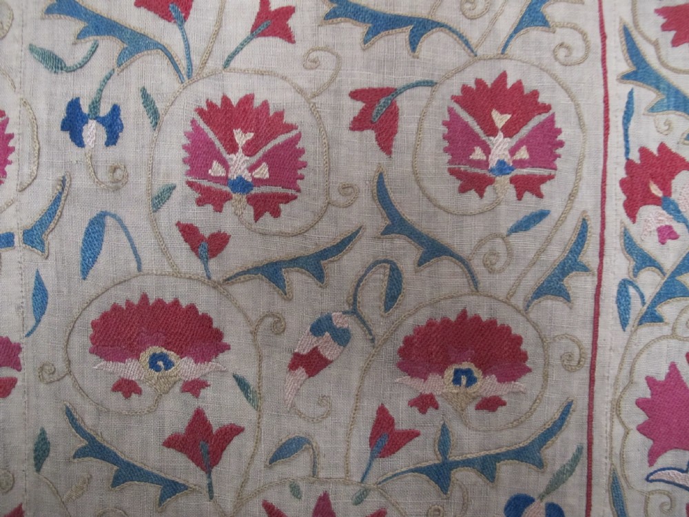 A rectangular antique silk-embroidered Suzani textile featuring crimson floral motifs and scrolling leaf borders on a beige cotton ground. View XII