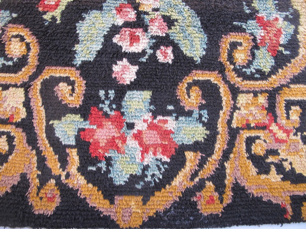 An early 20th-century Scandinavian Rya wool rug featuring a central floral bouquet in yellow, red, and green with scrollwork borders on a black field. View II