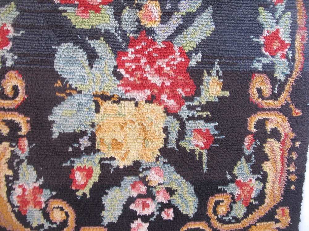 An early 20th-century Scandinavian Rya wool rug featuring a central floral bouquet in yellow, red, and green with scrollwork borders on a black field. View III