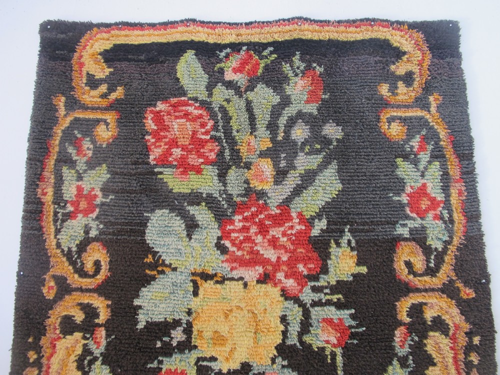 An early 20th-century Scandinavian Rya wool rug featuring a central floral bouquet in yellow, red, and green with scrollwork borders on a black field. View IV