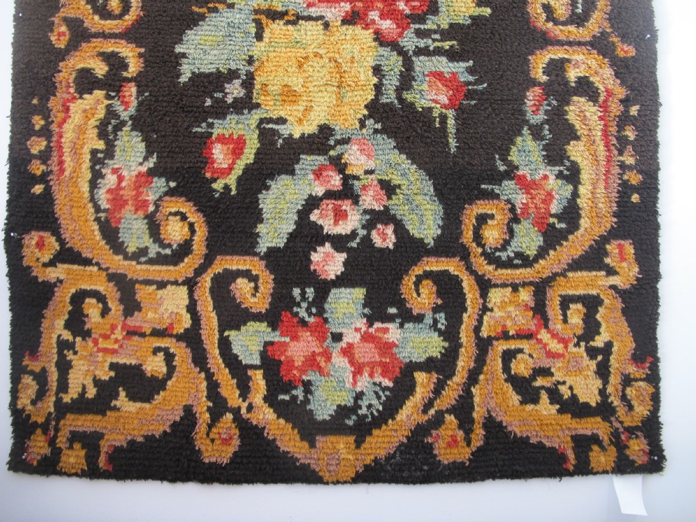An early 20th-century Scandinavian Rya wool rug featuring a central floral bouquet in yellow, red, and green with scrollwork borders on a black field. View V