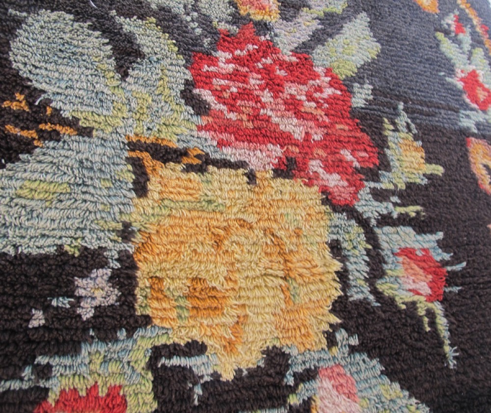 An early 20th-century Scandinavian Rya wool rug featuring a central floral bouquet in yellow, red, and green with scrollwork borders on a black field. View VI